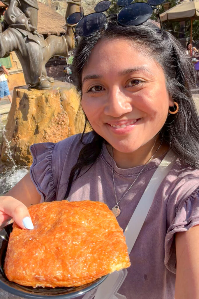 Guest holding crème brûlée croissant from Gaston’s Tavern at Magic Kingdom